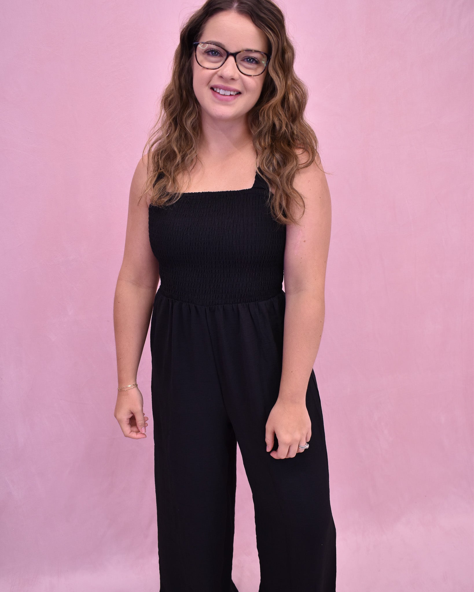 Woman wearing a black jumpsuit against a pink background