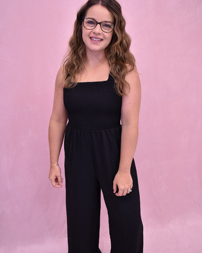Woman wearing a black jumpsuit against a pink background