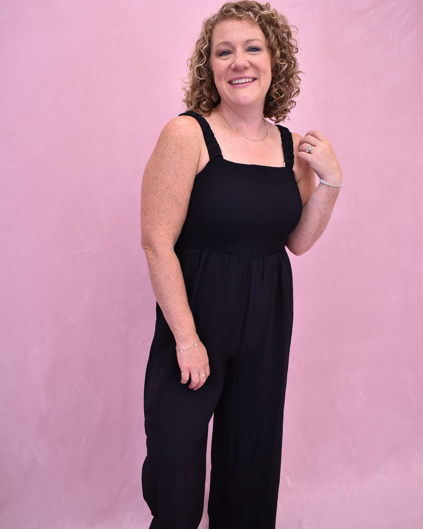 Woman wearing a black sleeveless jumpsuit against a pink background