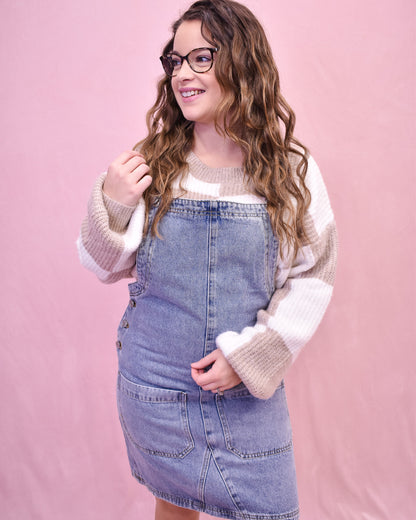 Woman wearing a denim dress and light sweater against a pink background