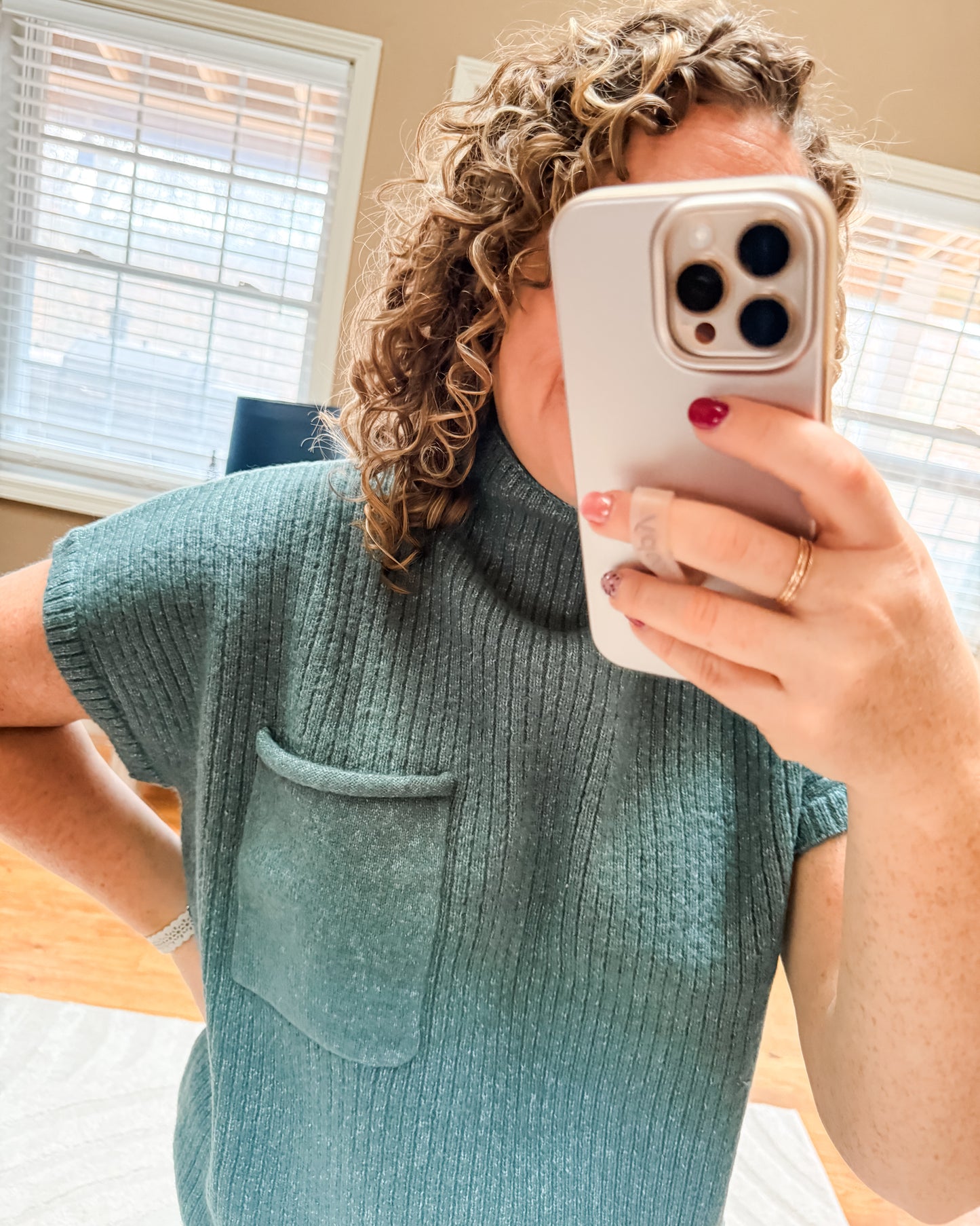 Person wearing a teal sweater taking a mirror selfie with a phone.