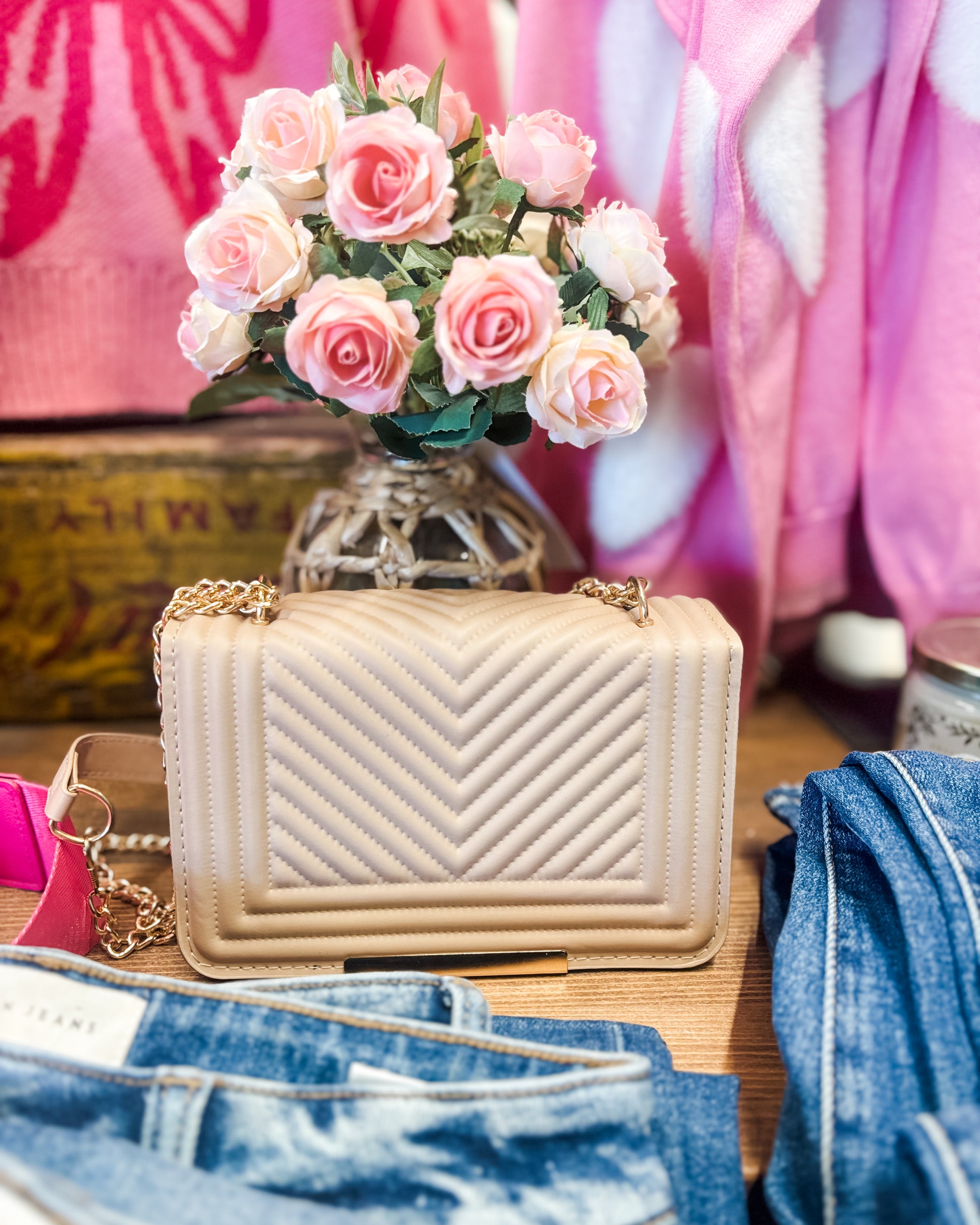 Beige quilted handbag with pink flowers and denim jeans on a wooden surface