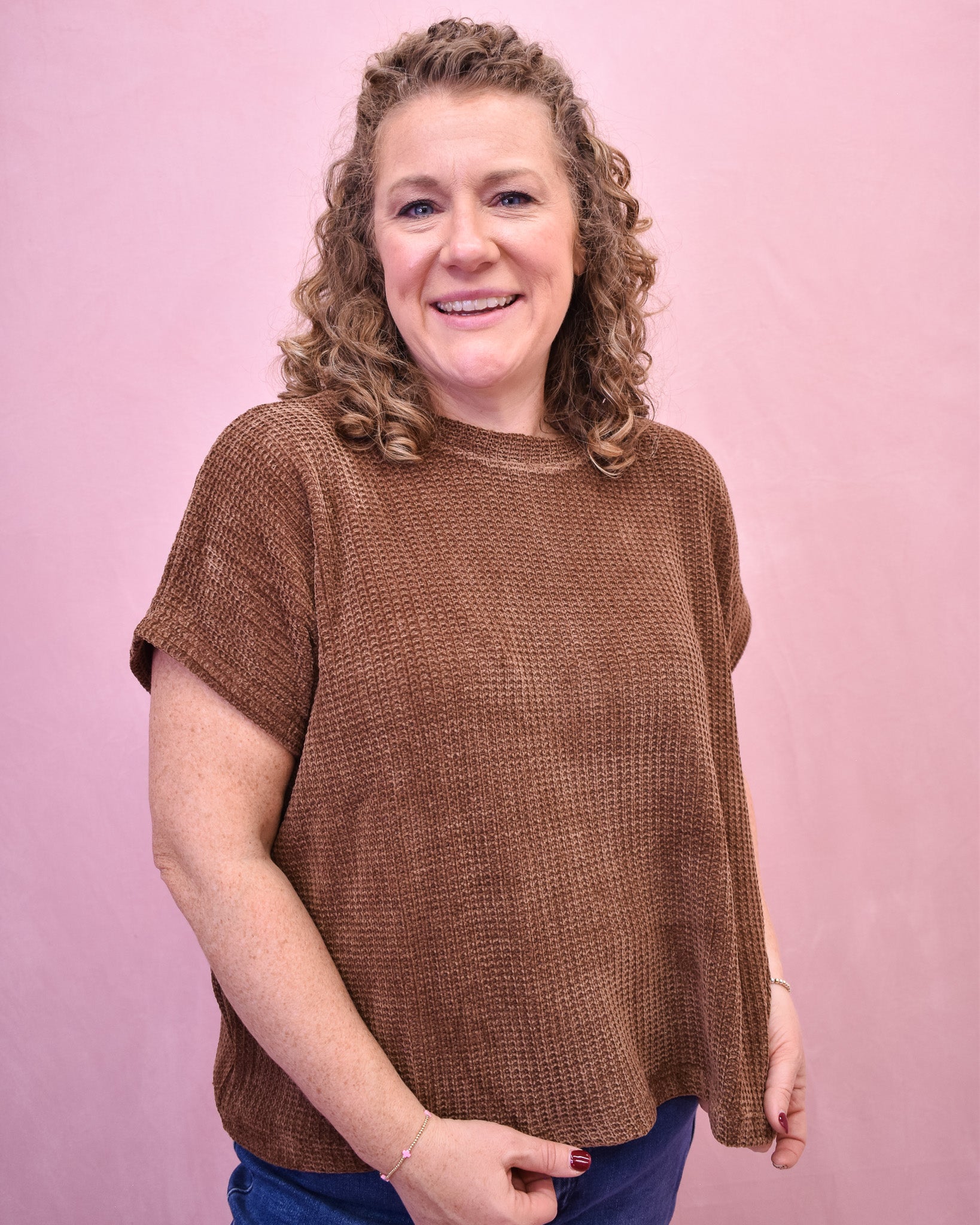 Woman wearing a brown knit top against a pink background