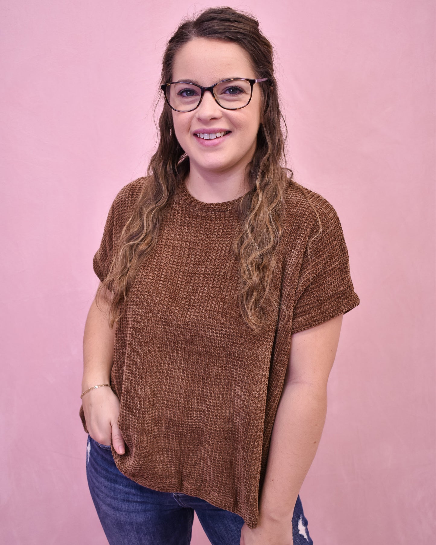 Woman wearing a brown textured sweater and glasses against a pink background