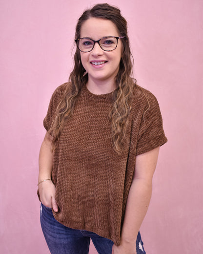 Woman wearing a brown textured sweater and glasses against a pink background