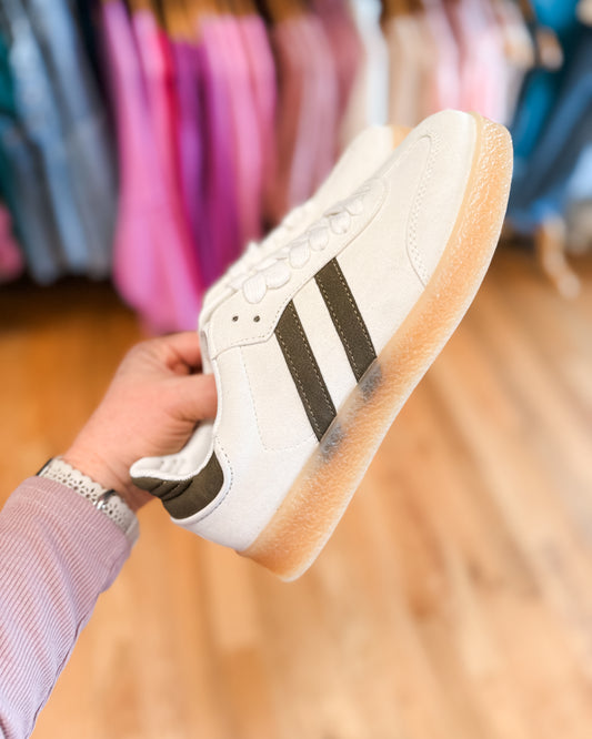 White sneaker with black stripes held by a person in a clothing store.