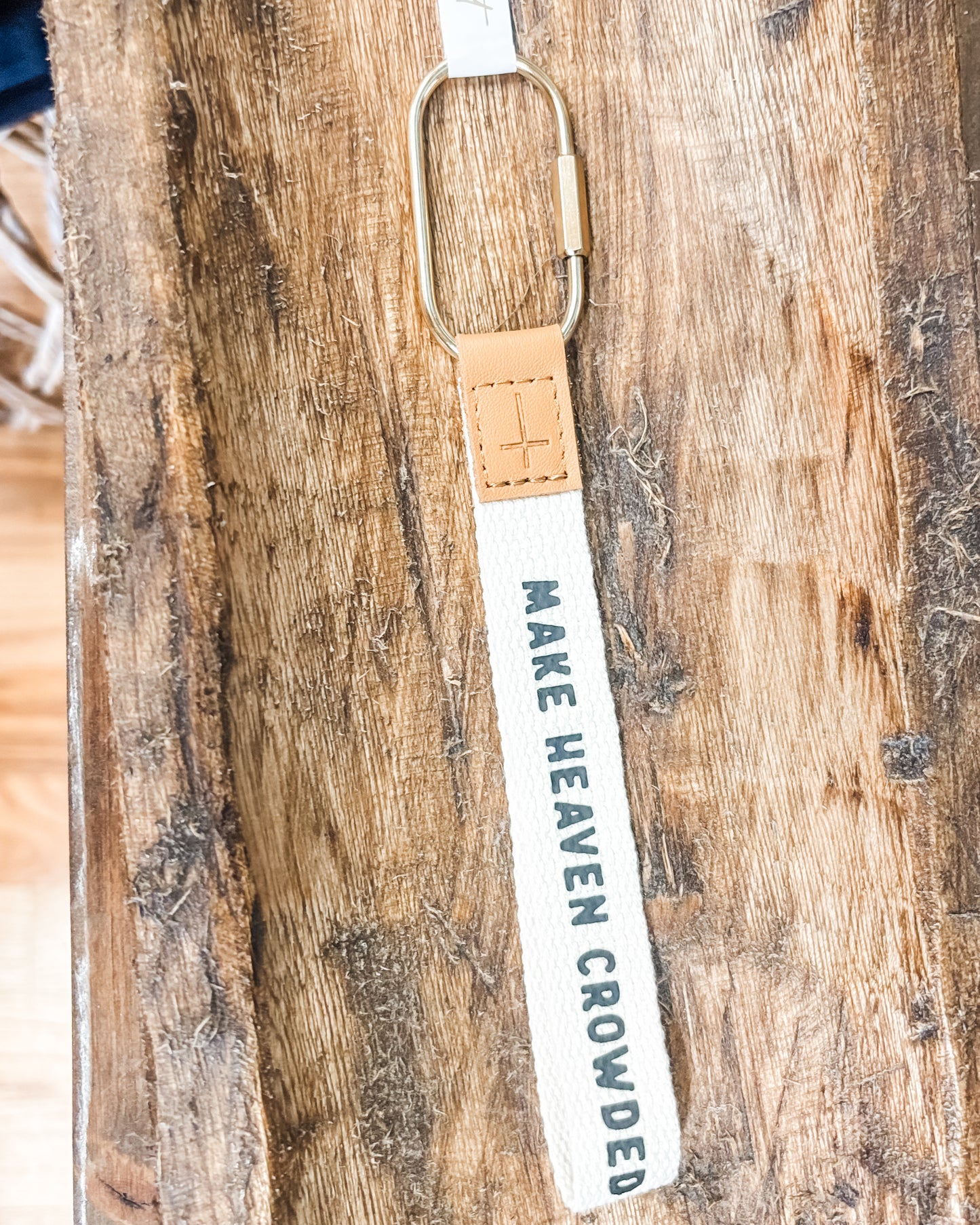 Keychain with 'MAKE HEAVEN CROWDED' text on a wooden surface