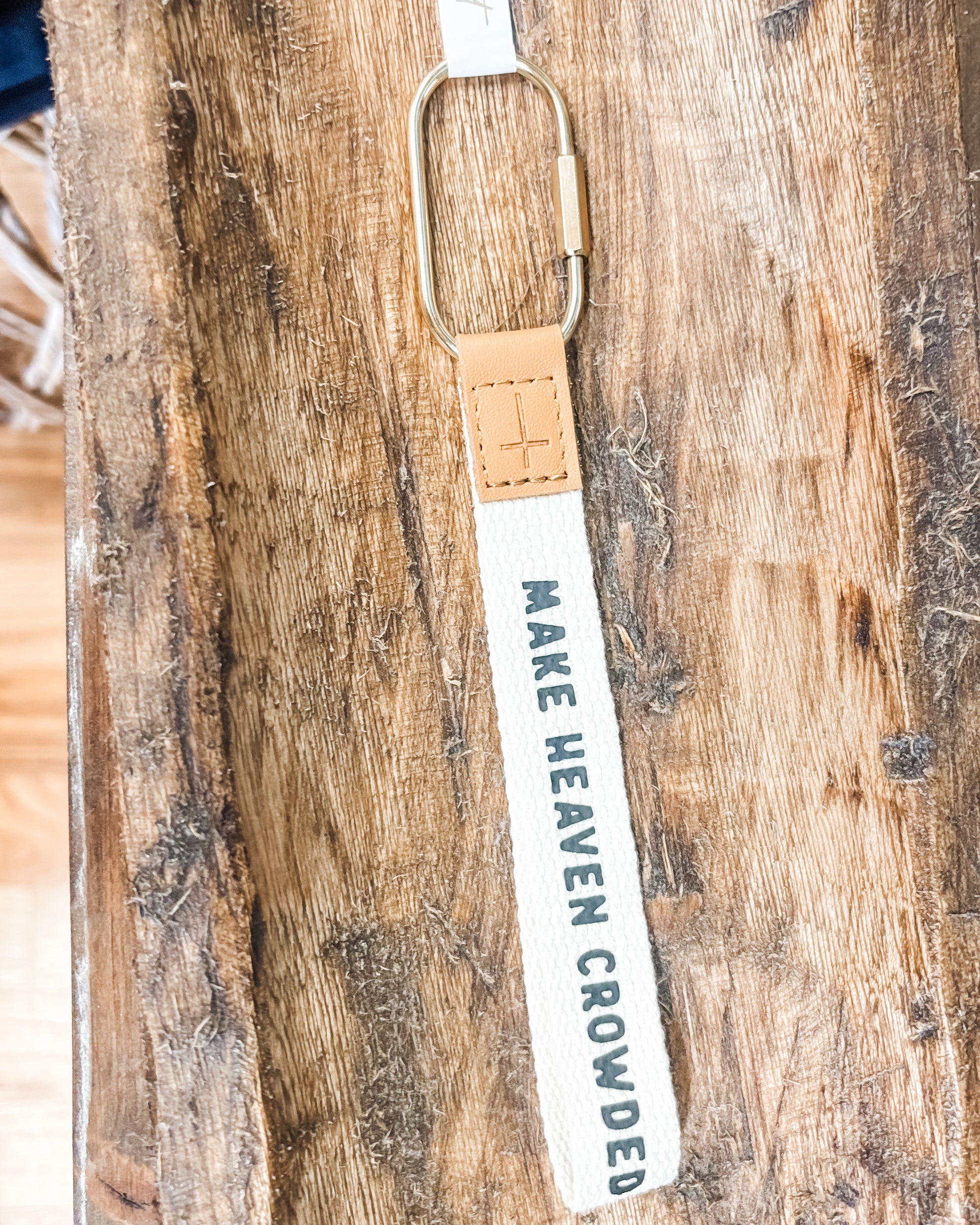 Keychain with 'MAKE HEAVEN CROWDED' text on a wooden surface