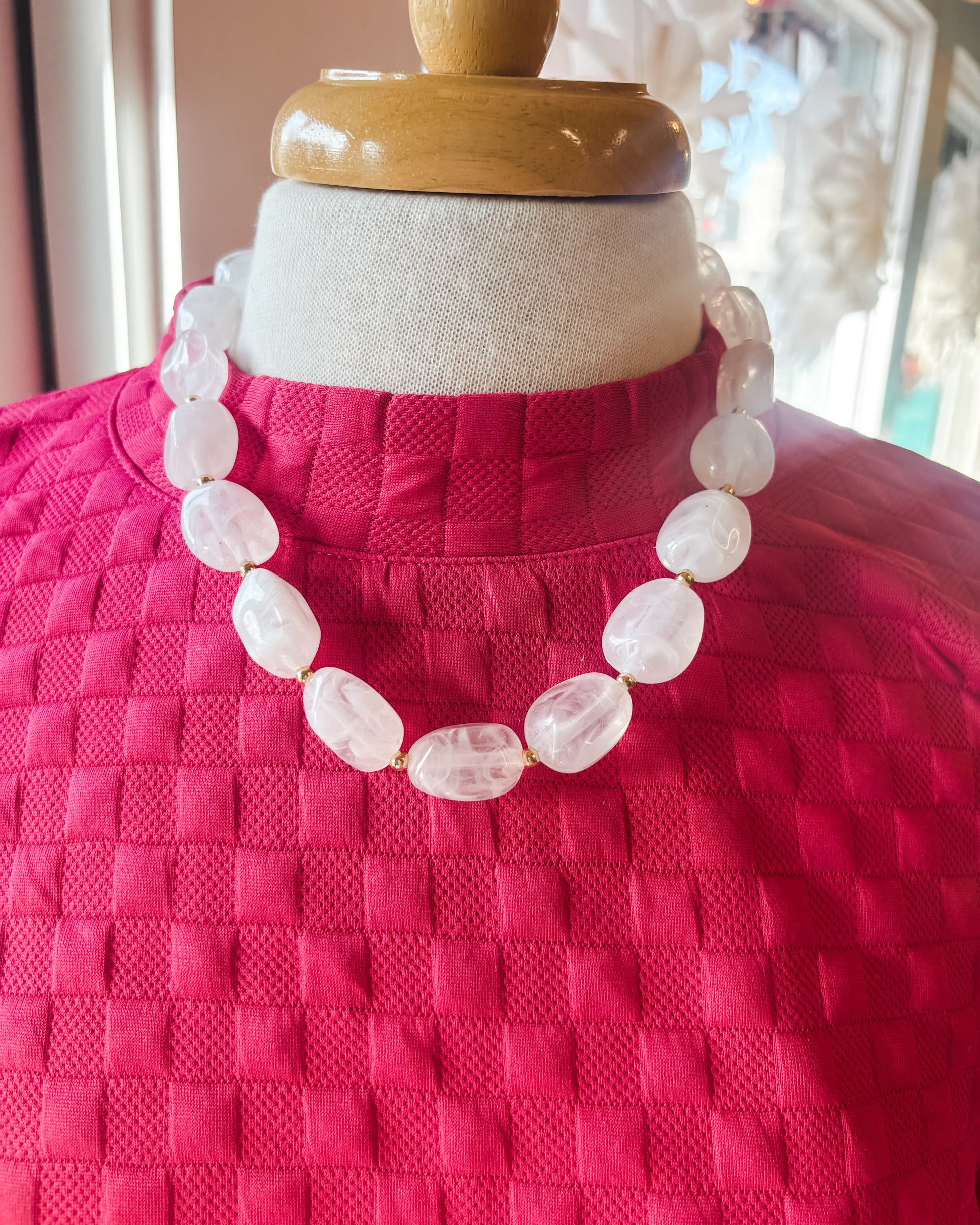 Necklace on a mannequin wearing a pink textured garment