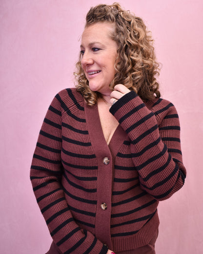 Woman wearing a brown and black striped cardigan against a pink background