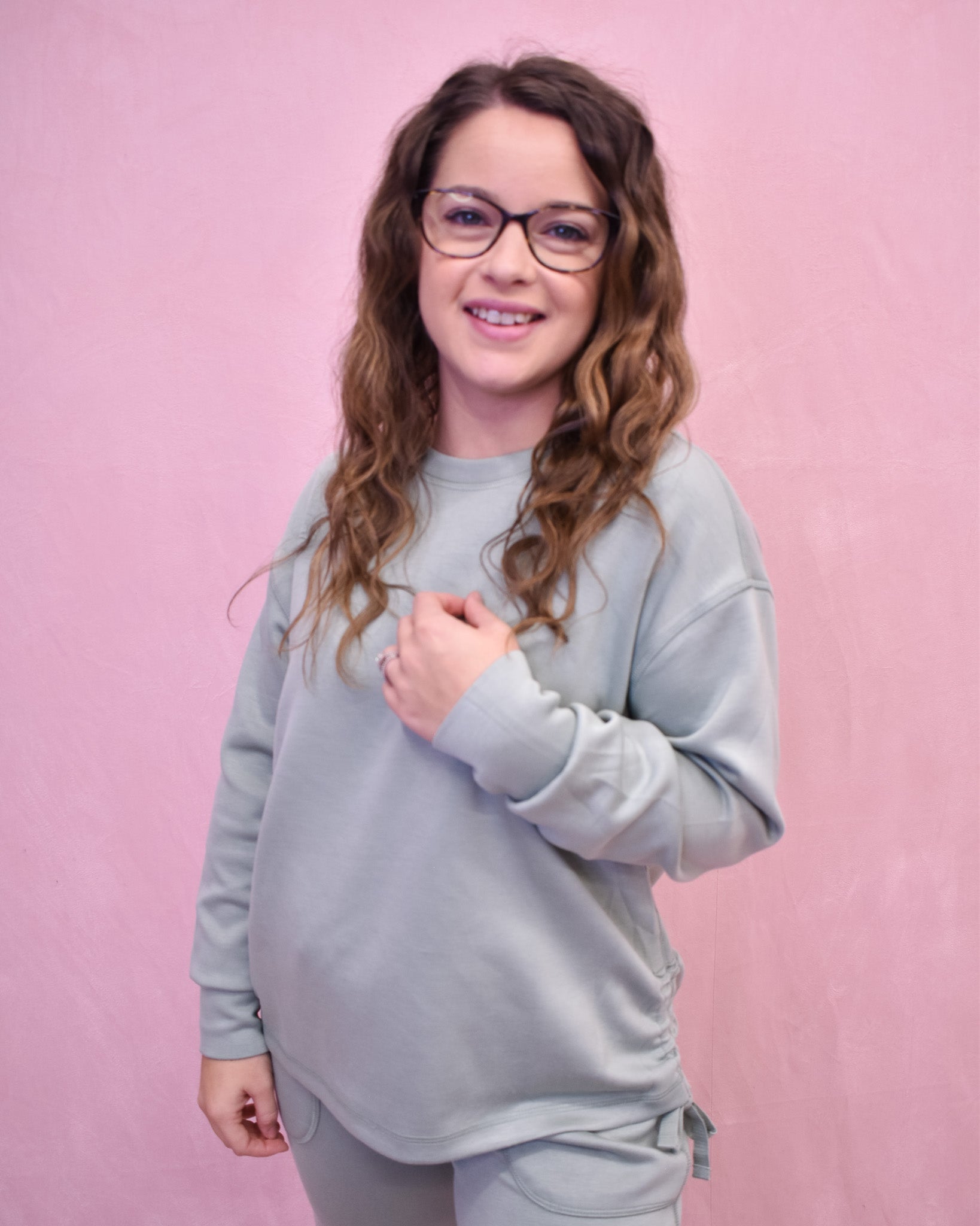 Woman wearing a light gray sweatshirt against a pink background