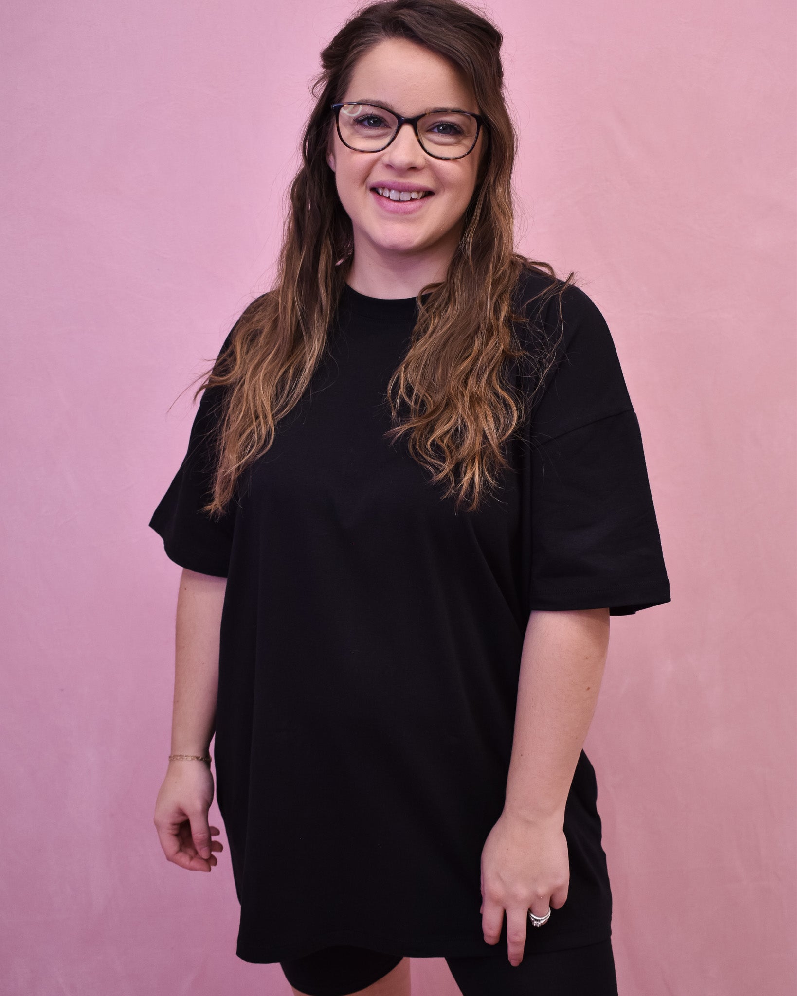 Person wearing a black oversized t-shirt against a pink background