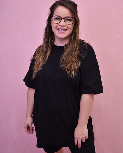 Person wearing a black oversized t-shirt against a pink background