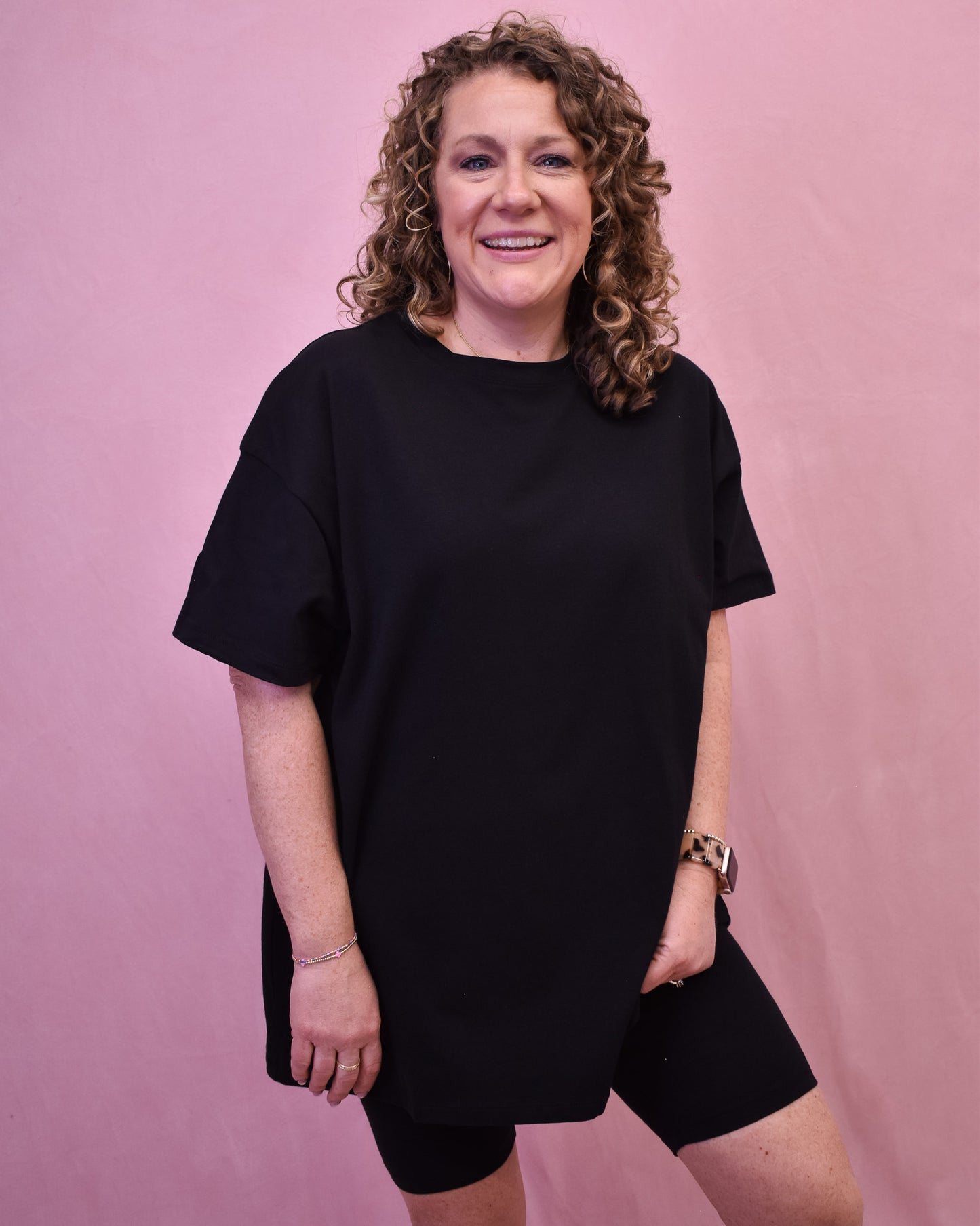 Person wearing a black outfit against a pink background