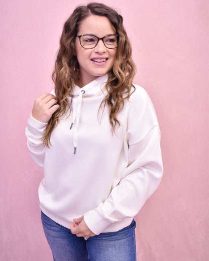 Person wearing a white hoodie and blue jeans against a pink background