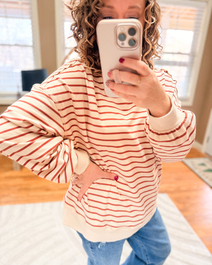 Person wearing a red and white striped sweater with a heart design, taking a mirror selfie.