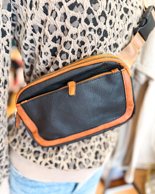 Black leather pouch with orange trim worn by a person in a leopard print top.