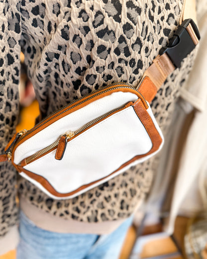 White handbag with brown leather strap and trim, worn by a person with leopard print fabric.