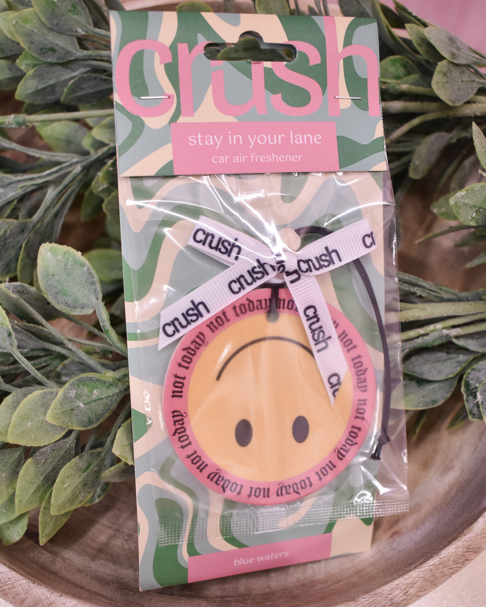 Packaged car air freshener with 'crush' branding on a wooden surface with green leaves.