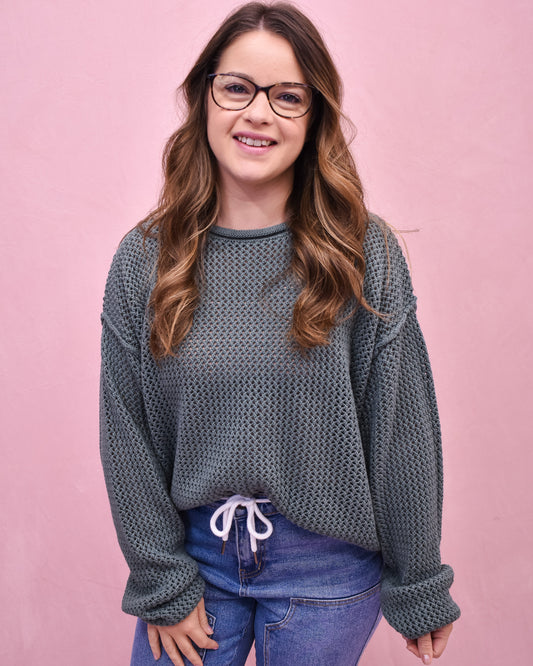 Woman wearing a textured gray sweater and blue jeans against a pink background