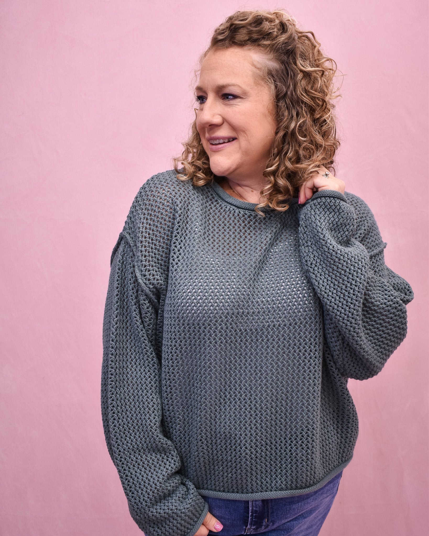 Woman wearing a textured gray sweater against a pink background