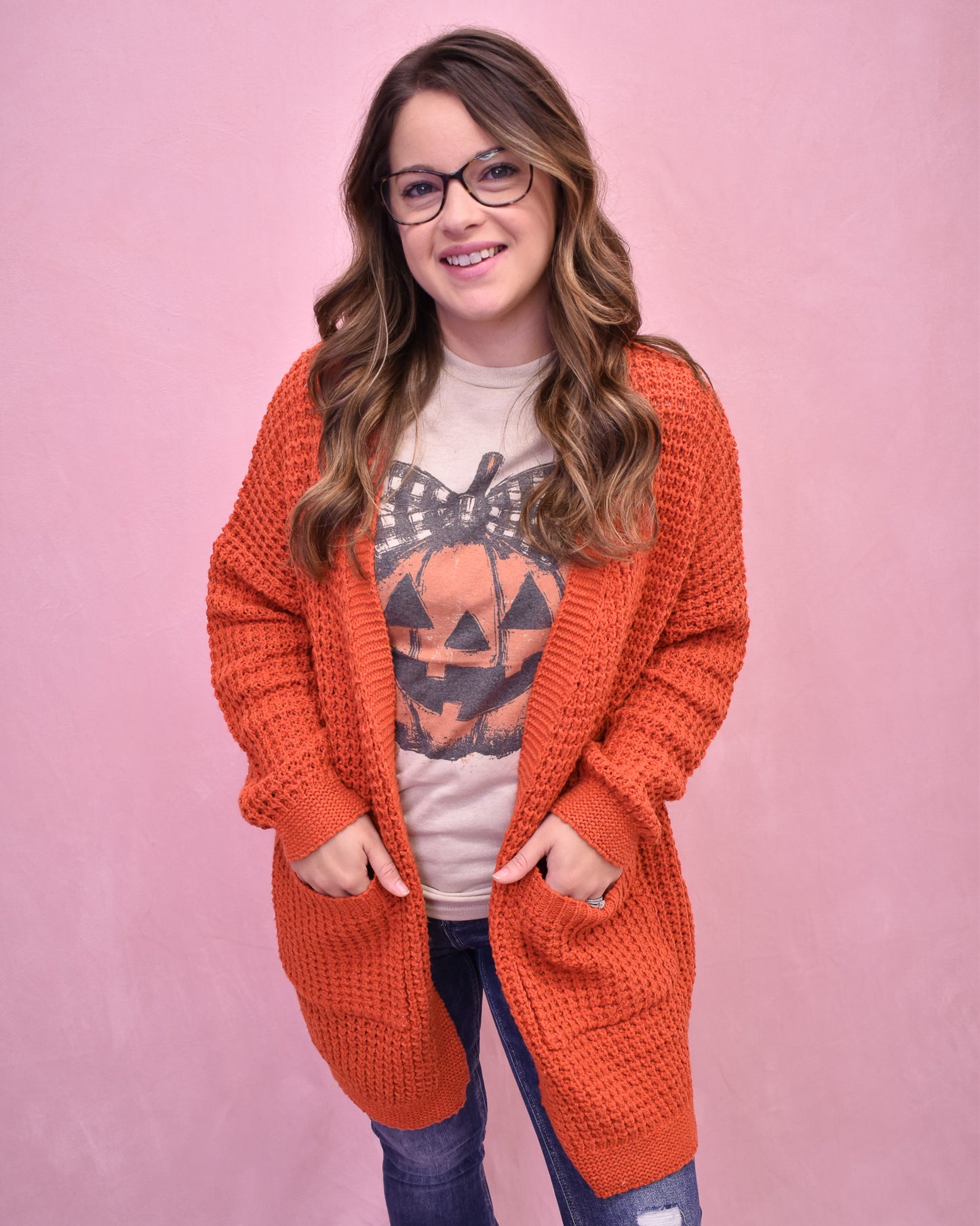 Woman wearing an orange cardigan over a Halloween-themed shirt on a pink background