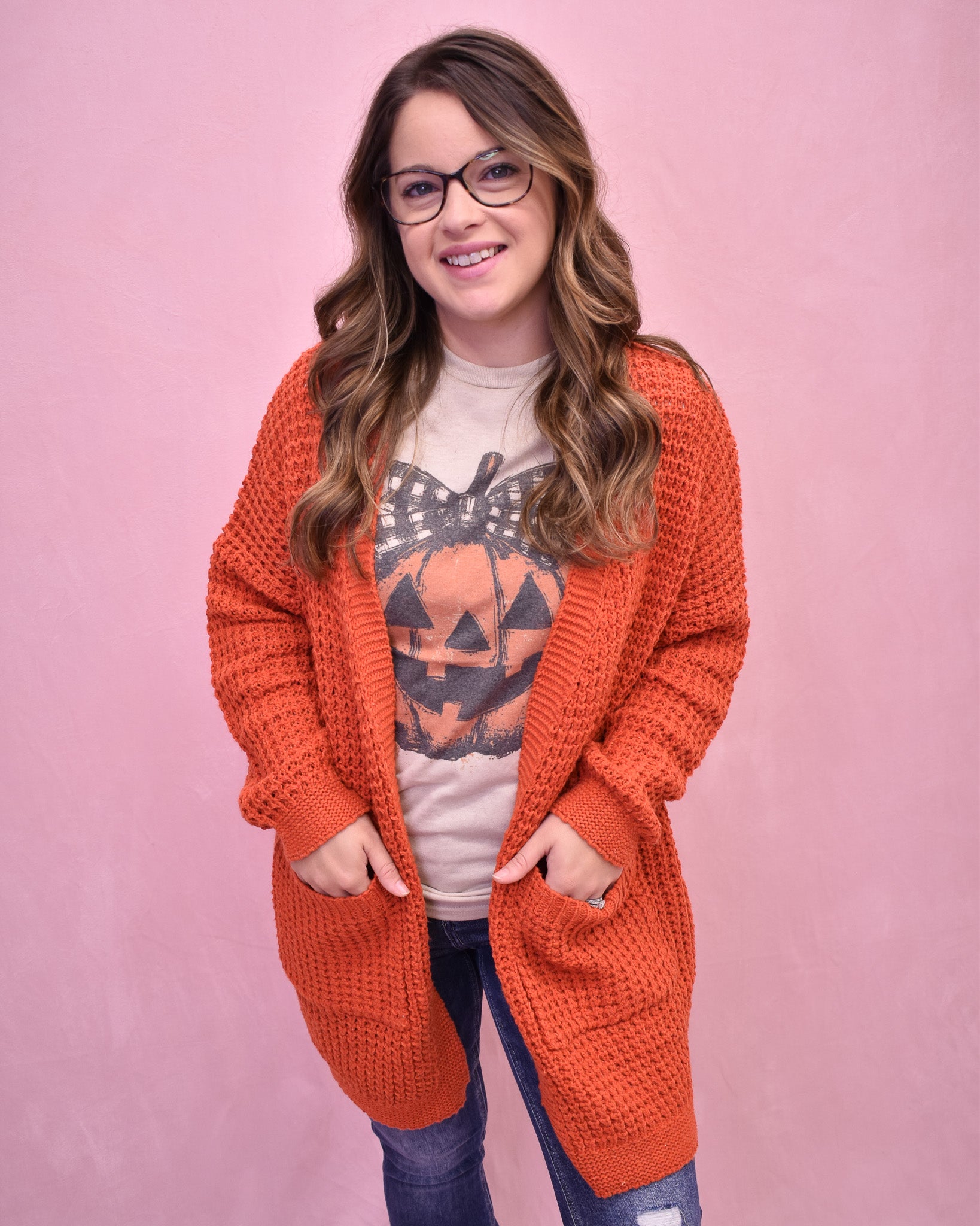 Woman wearing an orange cardigan over a Halloween-themed shirt on a pink background