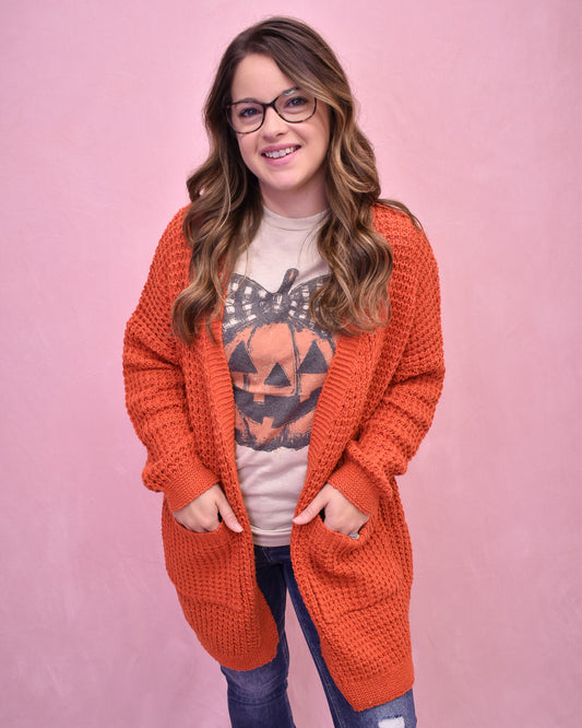 Woman wearing an orange cardigan over a Halloween-themed shirt on a pink background
