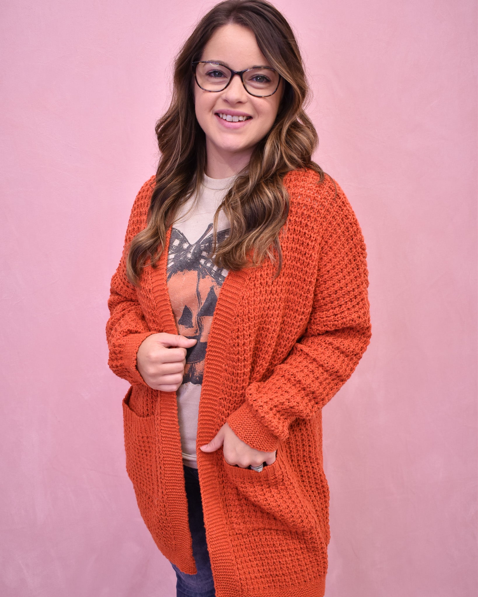 Woman wearing an orange knitted cardigan against a pink background