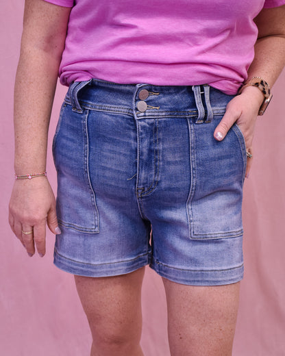 Person wearing blue denim shorts and a pink shirt on a pink background
