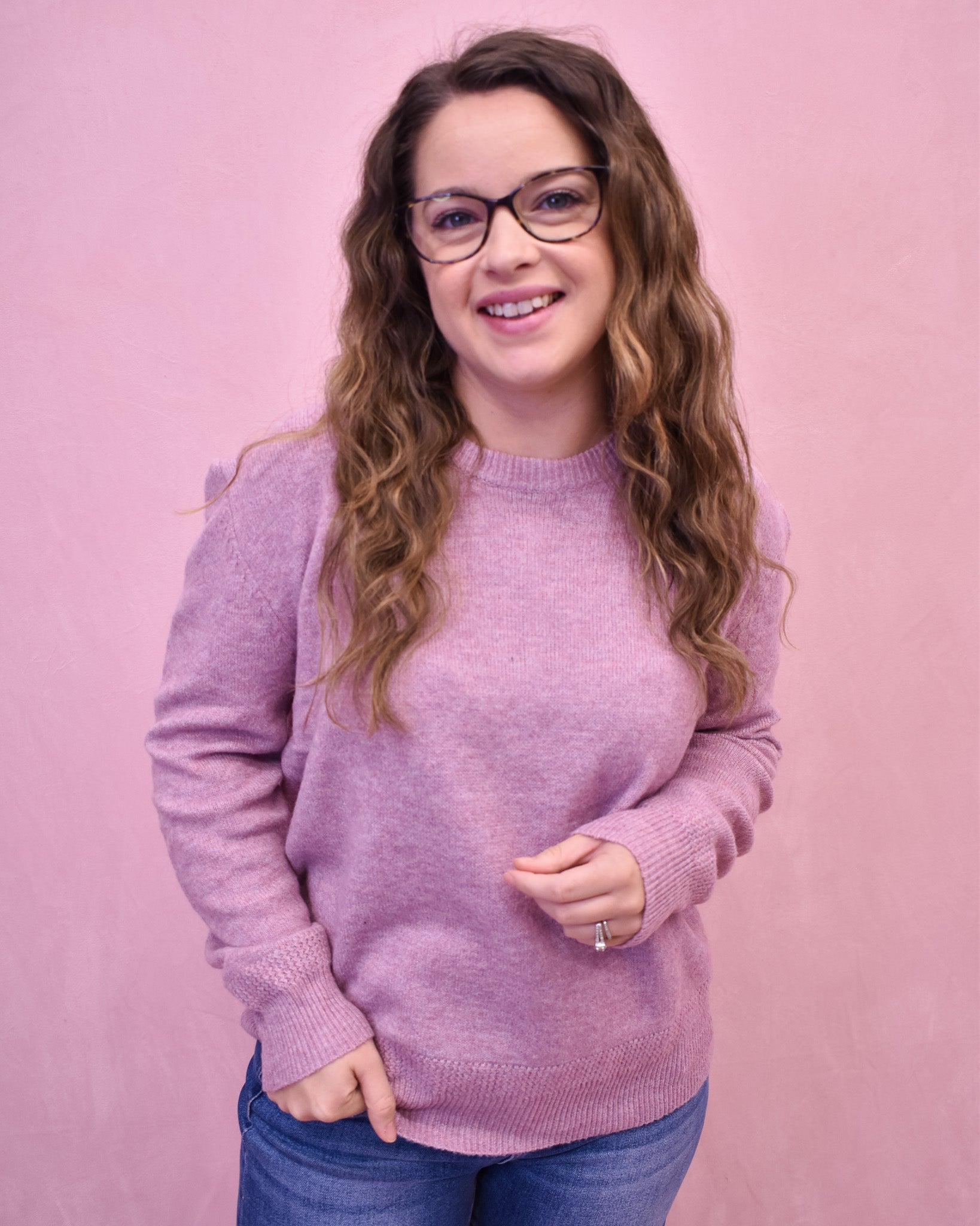 Woman wearing a pink sweater and glasses against a pink background