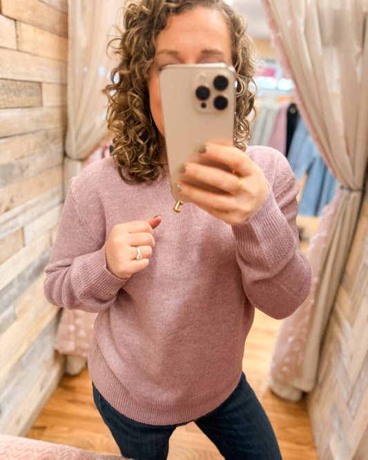 Person wearing a pink sweater taking a mirror selfie.