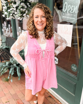 a pink denim shorts romper with pleated vneck and front tie. Paired with a basic lace layering top.