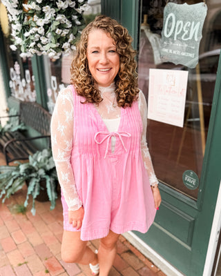 a pink denim shorts romper with pleated vneck and front tie. Paired with a basic lace layering top.