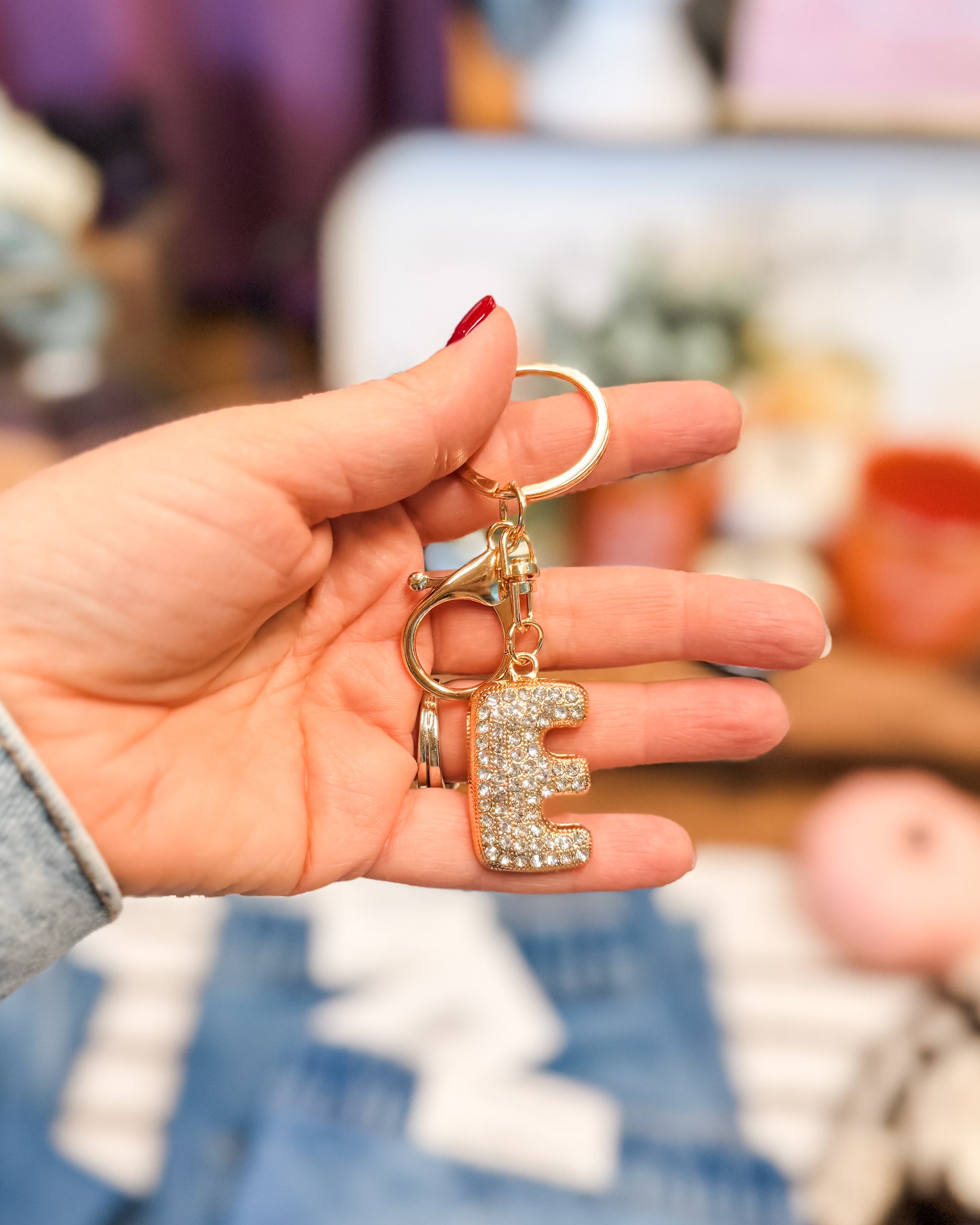 Hand holding a keychain with a letter 'E' charm against a blurred background