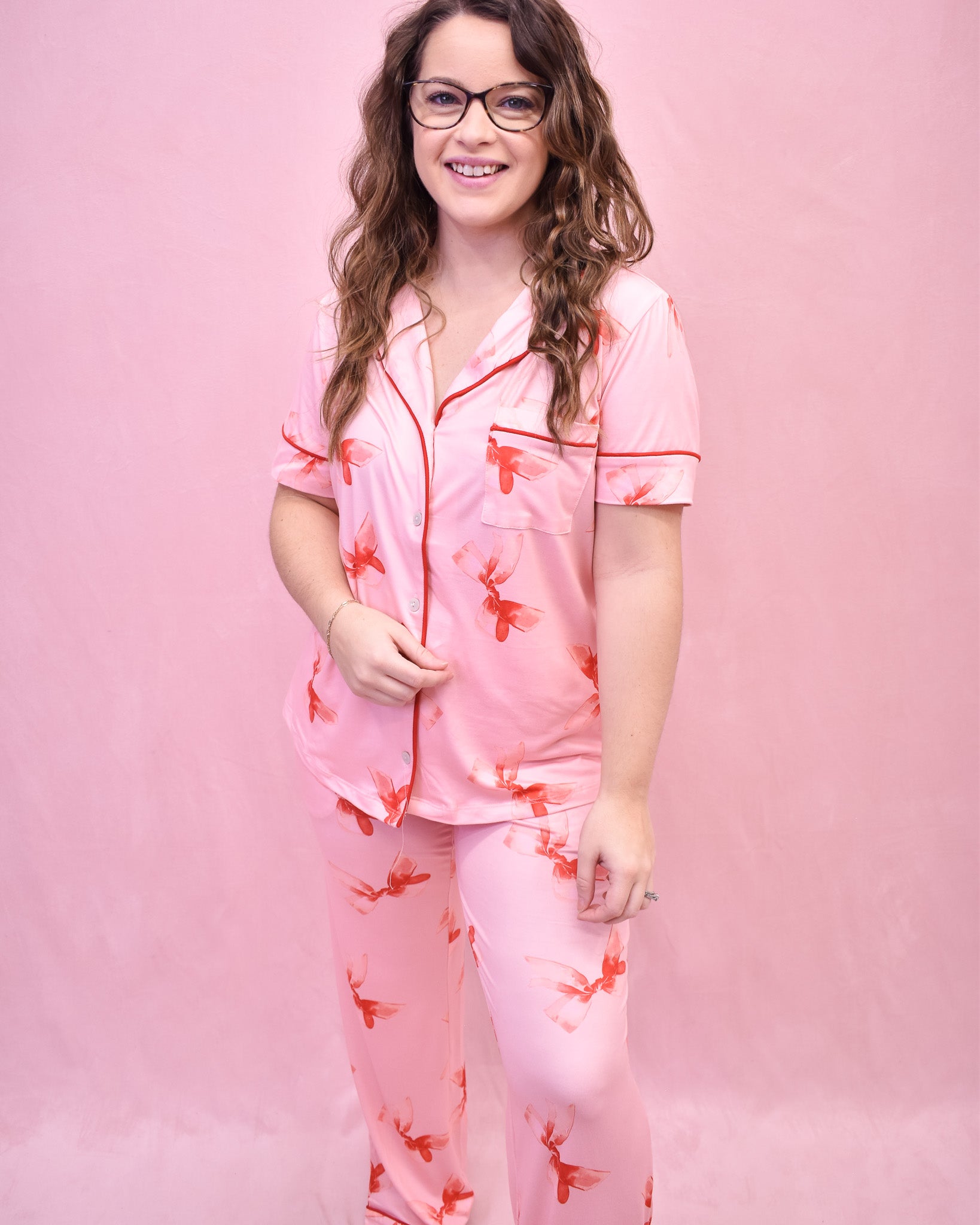 Woman wearing a pink pajama set with red floral patterns against a pink background
