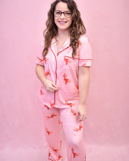 Woman wearing a pink pajama set with red floral patterns against a pink background