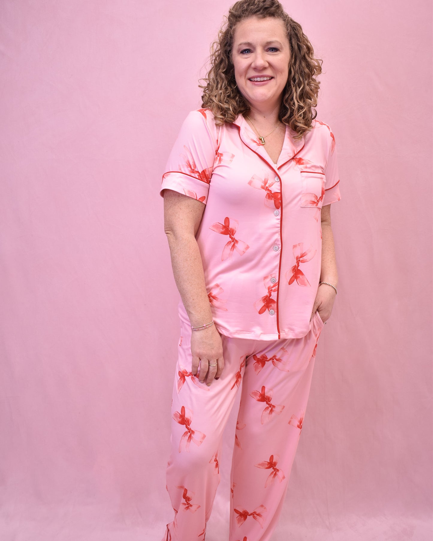 Woman wearing pink pajamas with red floral patterns against a pink background