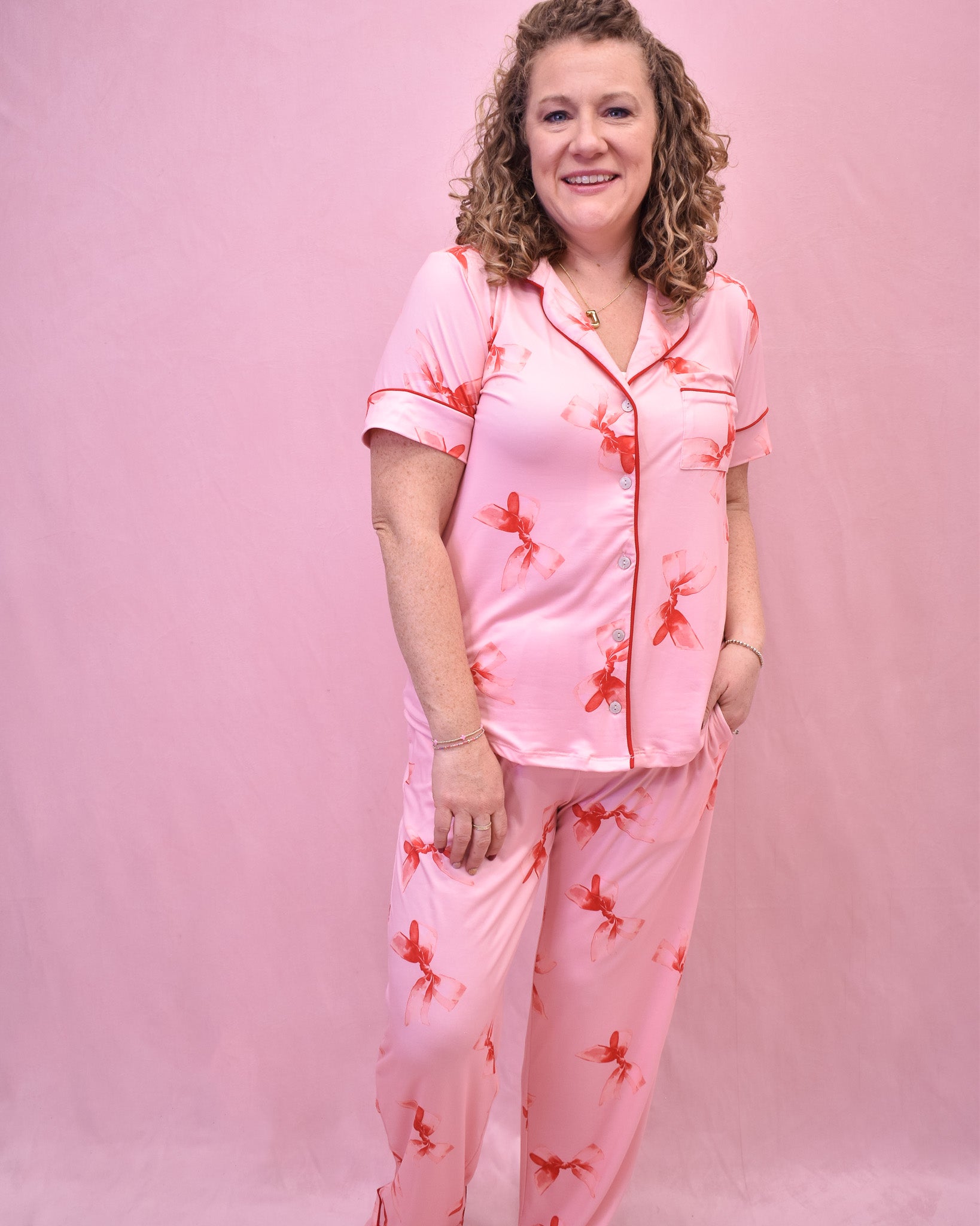 Woman wearing pink pajamas with red floral patterns against a pink background
