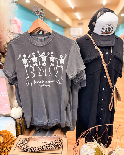 Gray t-shirt with skeleton design and text, black jacket, white cap, and leopard print flats on a store display.