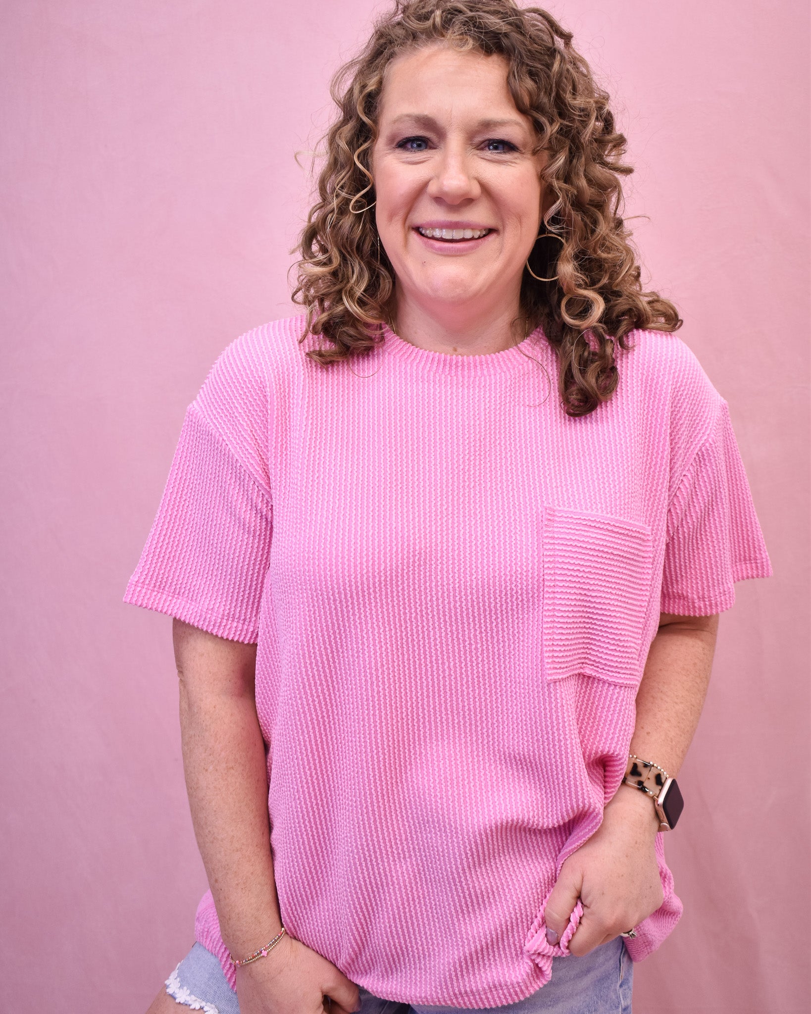 Person wearing a pink ribbed t-shirt against a pink background