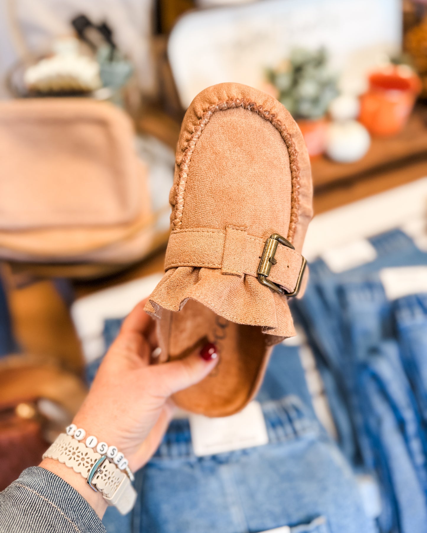 Tan slipper with a buckle held by a hand in a store setting