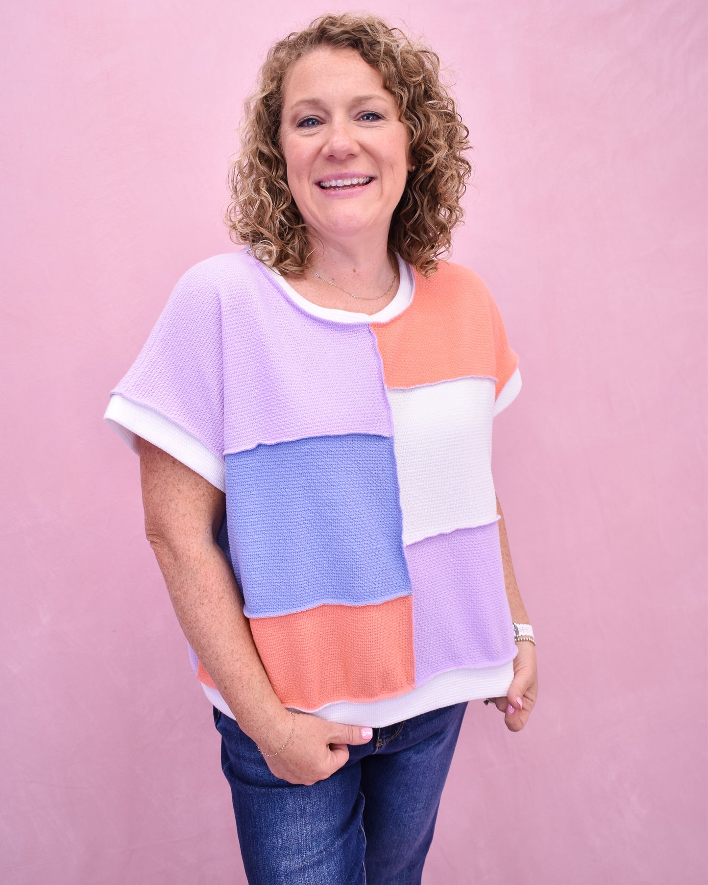 Woman wearing a colorful block-patterned shirt against a pink background