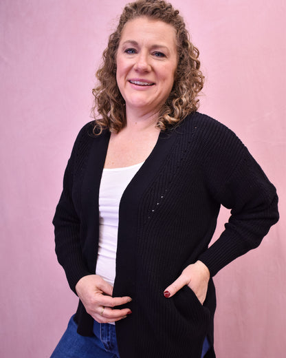 Woman wearing a black cardigan over a white top against a pink background