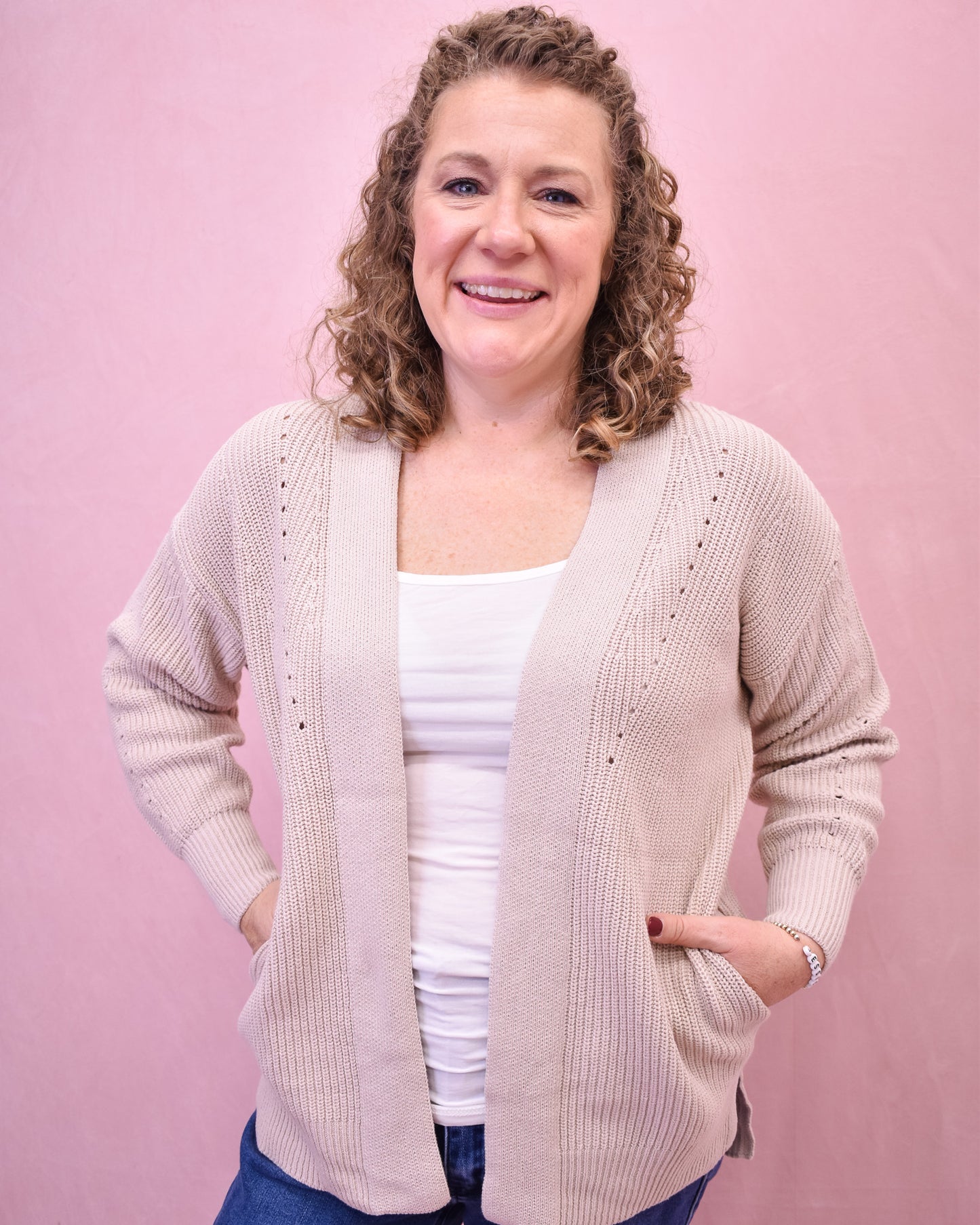 Woman wearing a beige cardigan over a white top against a pink background