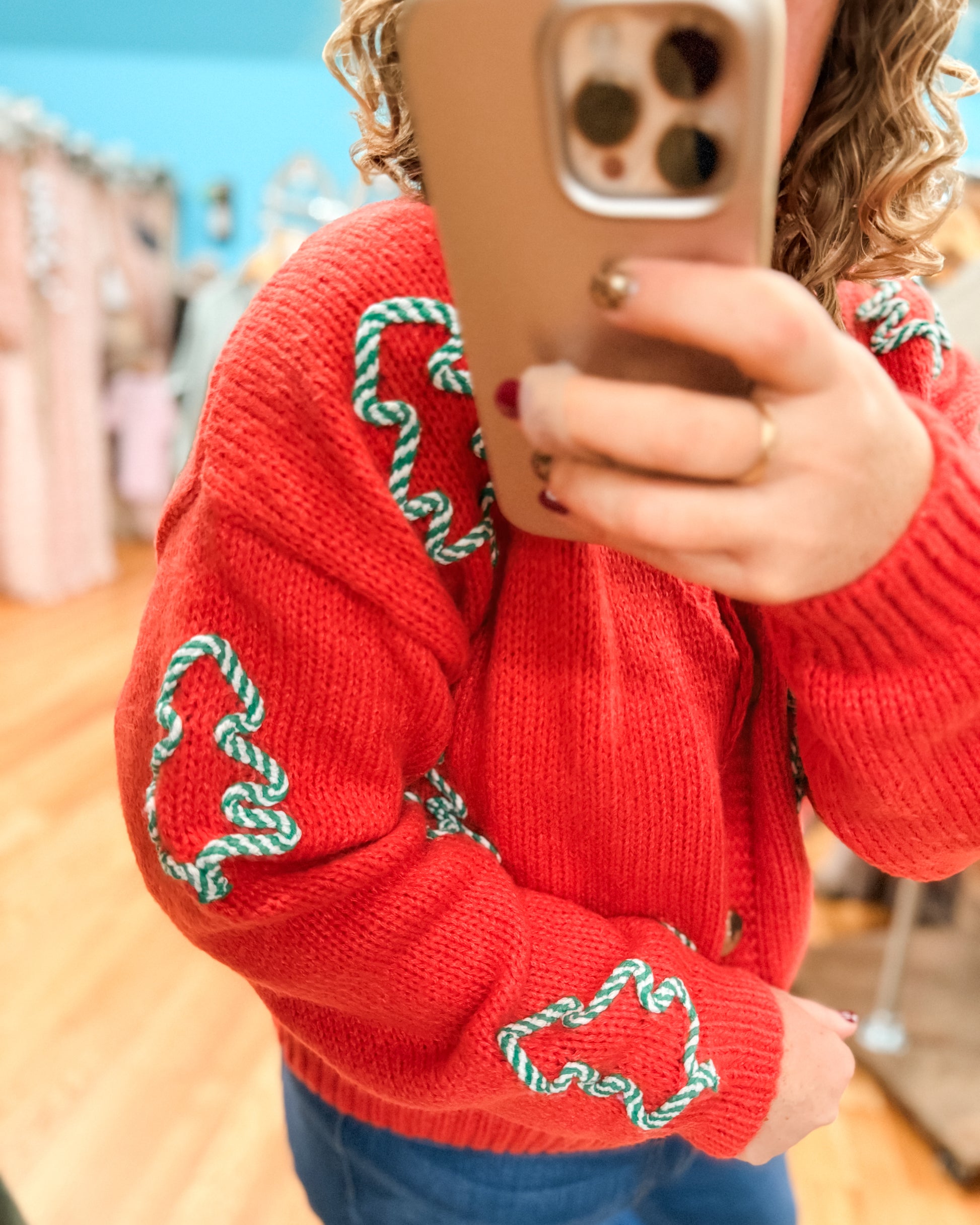 Person wearing a red sweater with green patterns, taking a mirror selfie.