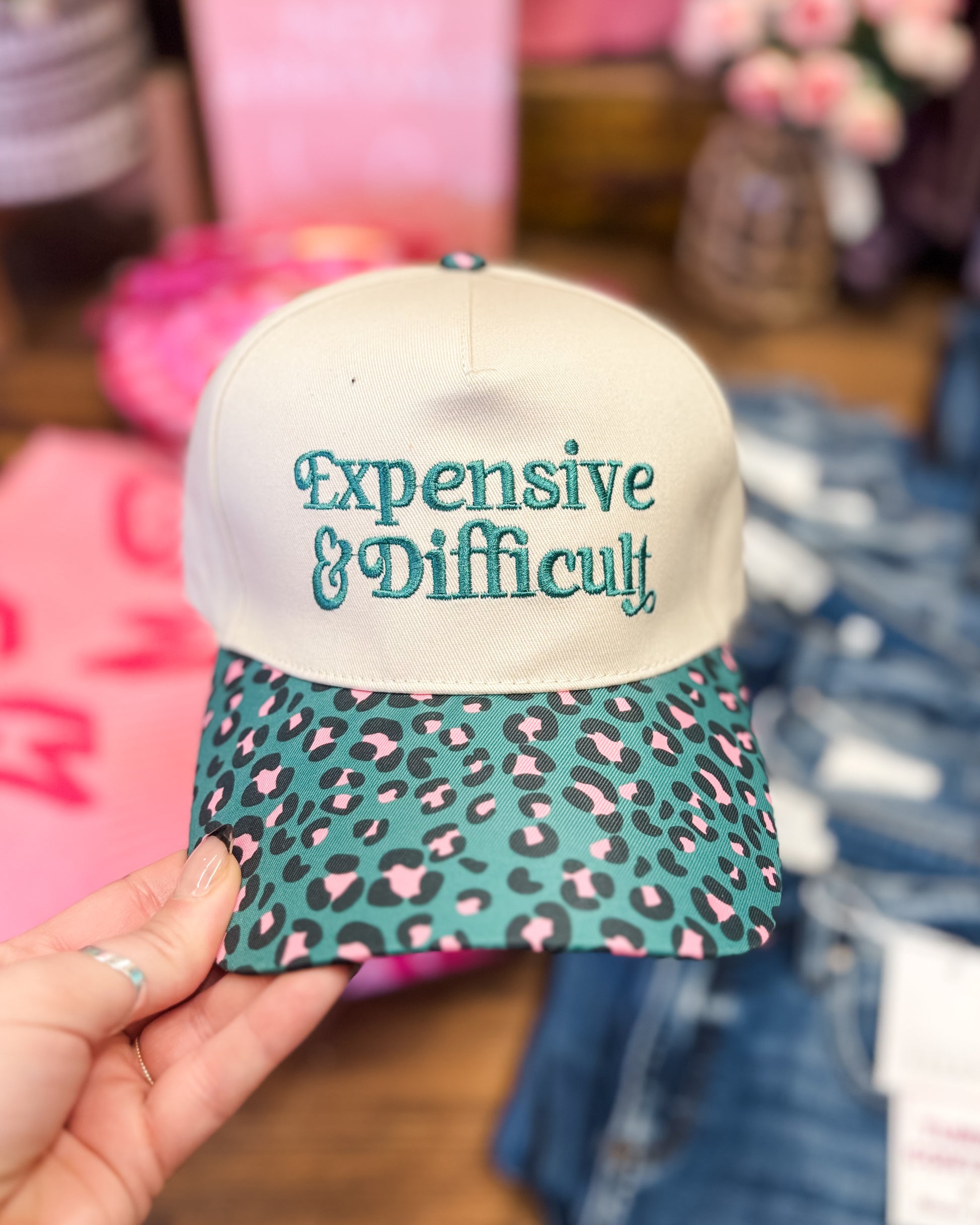 Cap with 'Expensive & Difficult' text and leopard print pattern held by a hand.