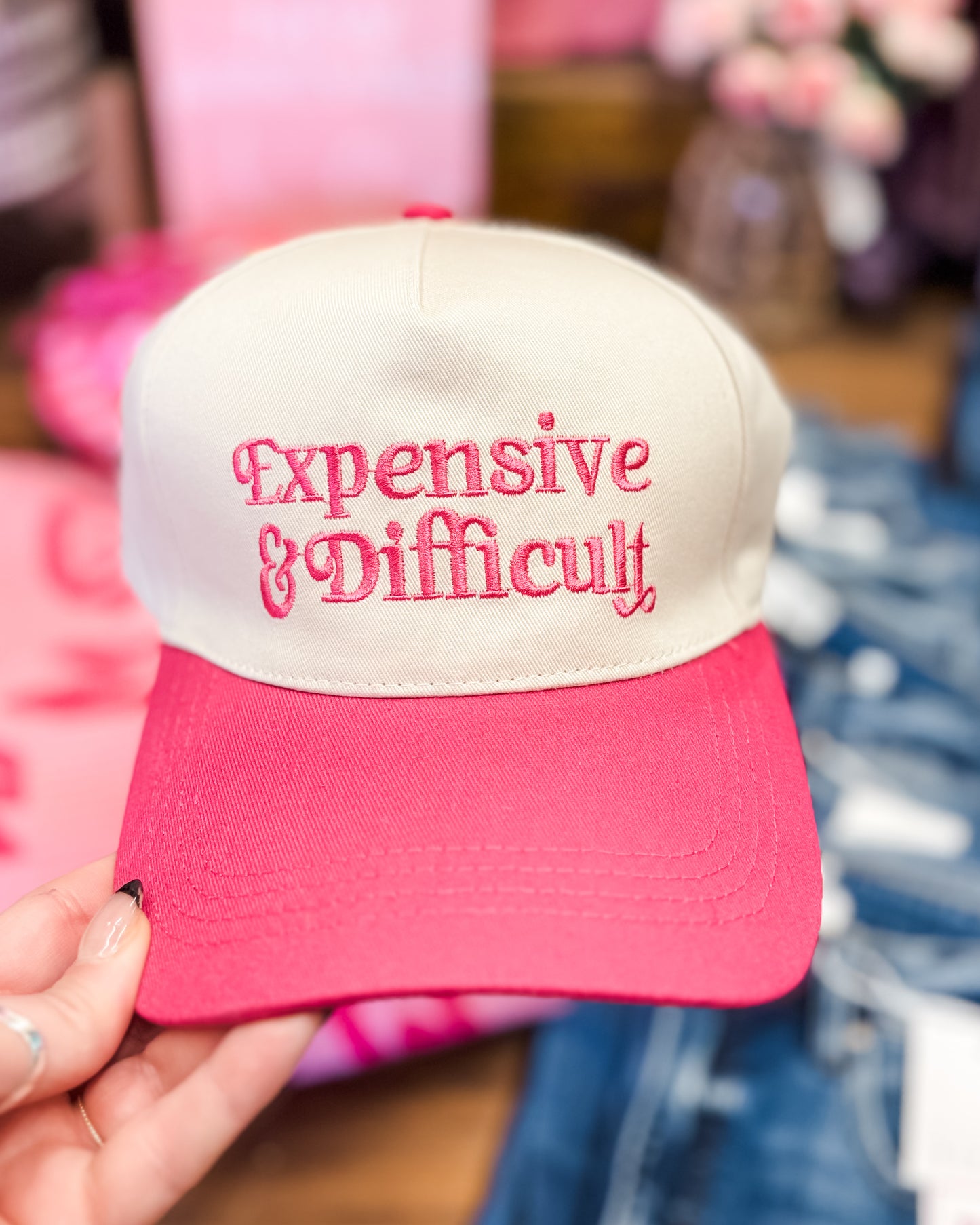 Pink and white cap with 'Expensive & Difficult' text held by a hand.