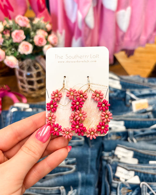 Pink floral earrings on a card held by a hand with denim and flowers in the background
