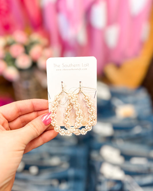 Hand holding a card with pearl earrings against a blurred background